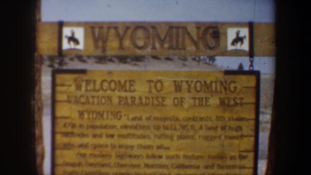 1957 8mm frame of a Wyoming welcome sign with cowboy silhouettes and readable vacation-state text.