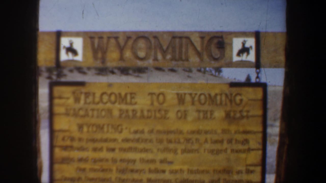 Soft 1957 Wyoming roadside sign frame showing the welcome message and western horseback silhouettes.