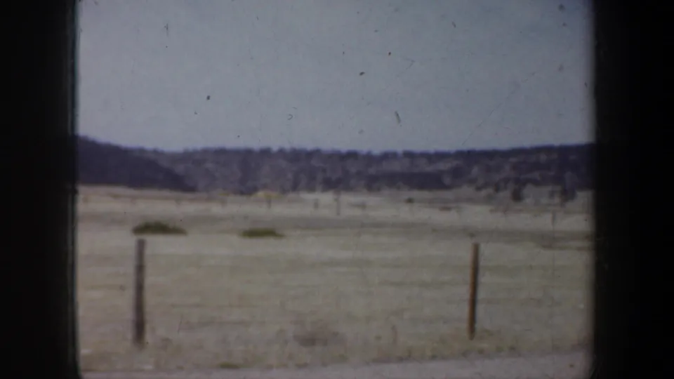 Final 1957 Wyoming 8mm frame showing open arid land, fence posts, distant hills, and visible film gate edges.