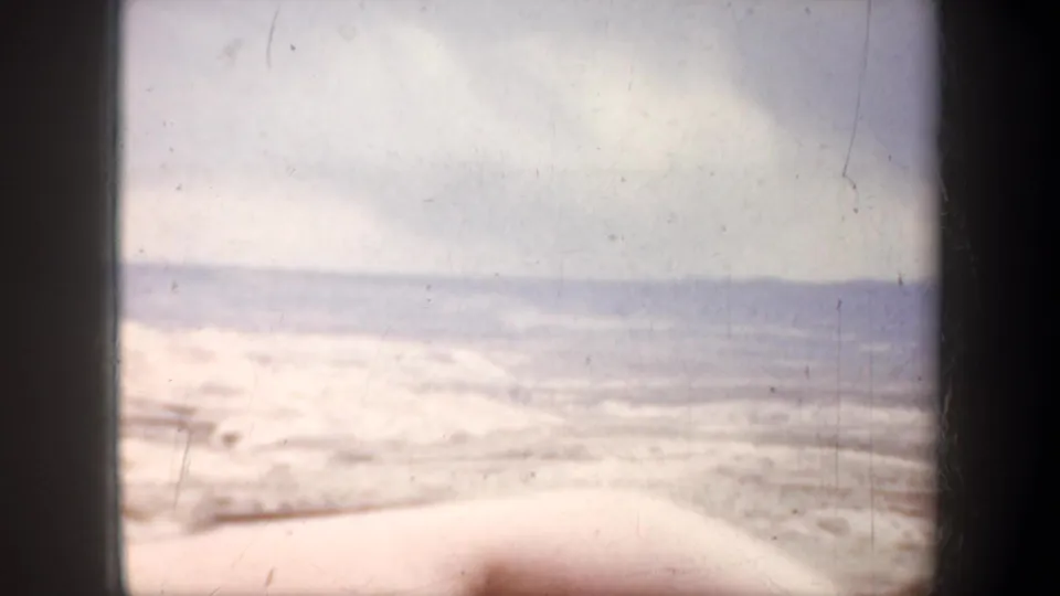 A bright 1957 Wyoming road-view frame shows open plain, pale clouds, distant hills, and car-edge foreground.