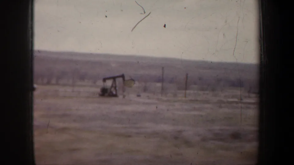 1957 Wyoming 8mm frame showing an oil pump jack set in open rural ground with fence posts, utility poles, and low hills.