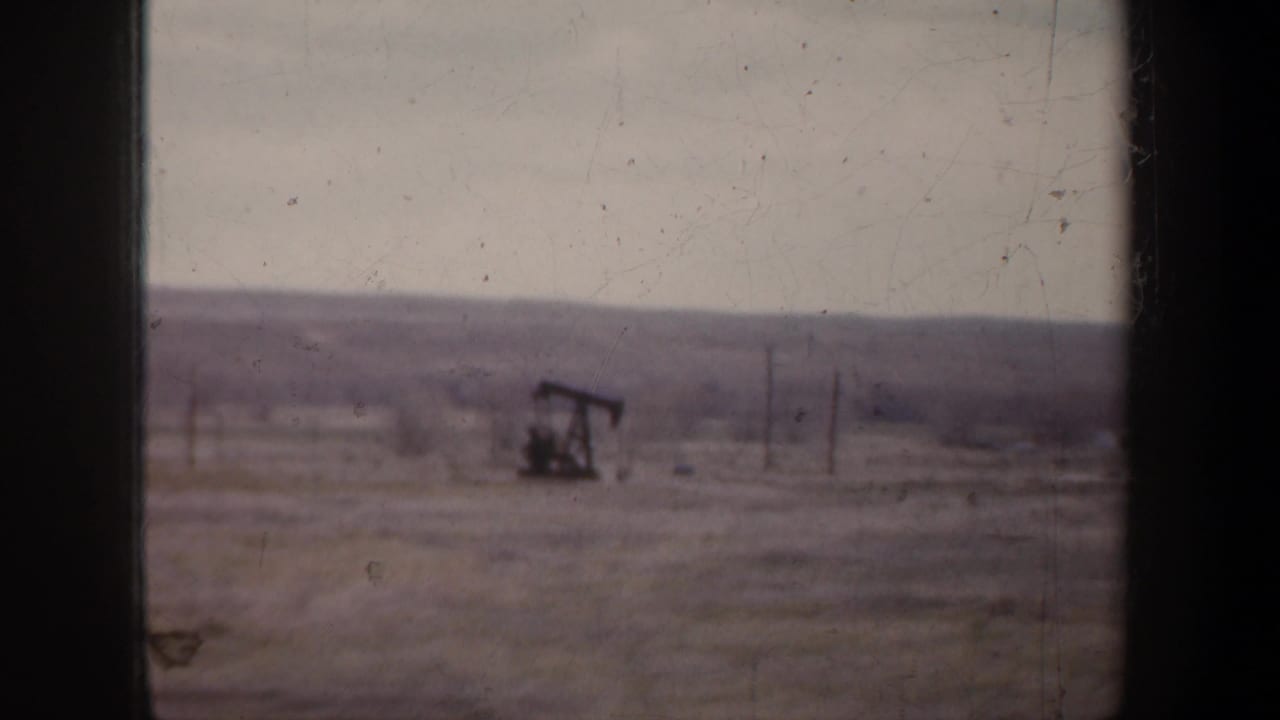 Oil pump jack in a flat rural field with low hills beyond.