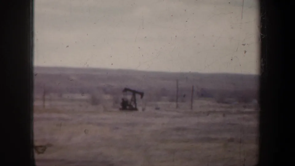 1957 Wyoming 8mm frame showing an oil pump jack in open countryside with utility poles and distant low hills.