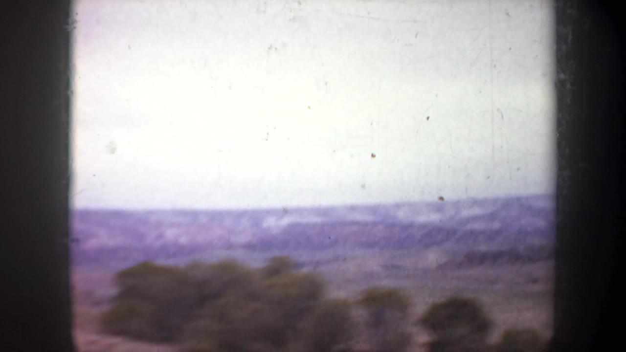 1957 Wyoming 8mm frame showing an aerial view across open scrubland toward hazy mountain ridges under a pale sky.