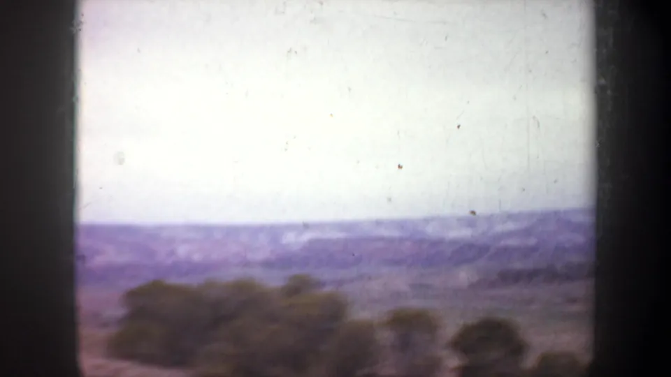 1957 Wyoming 8mm frame showing an aerial view across open scrubland toward hazy mountain ridges under a pale sky.