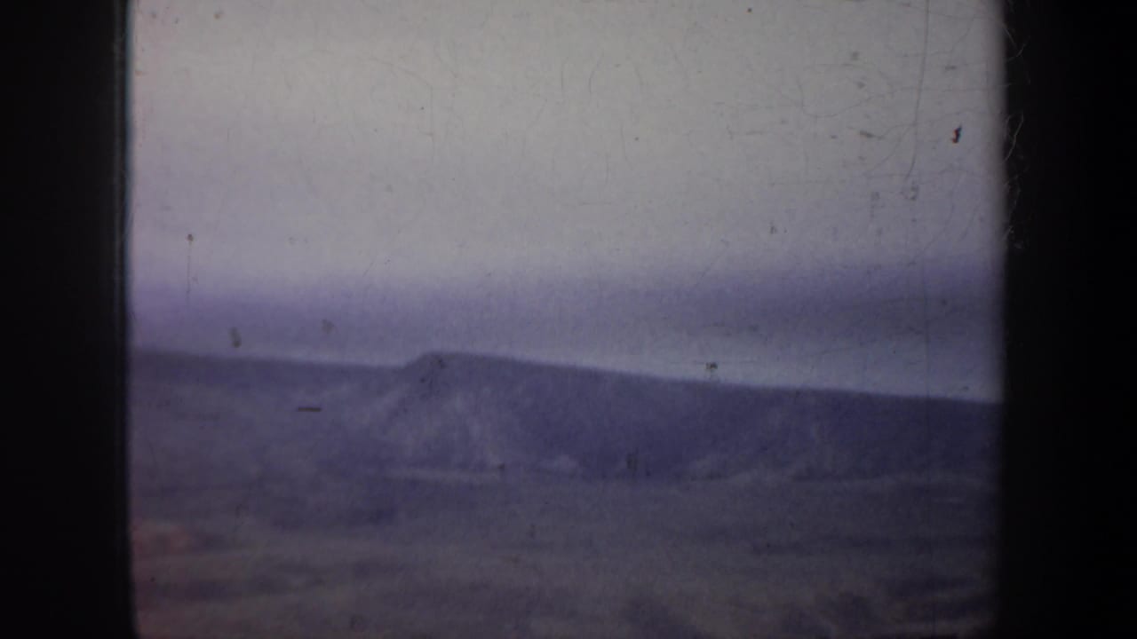 Aerial 8mm view in Wyoming with a low mountain ridge, broad valley floor, pale sky, and dark edges from the film or aircraft window.
