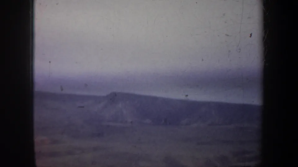 Aerial 8mm view in Wyoming with a low mountain ridge, broad valley floor, pale sky, and dark edges from the film or aircraft window.
