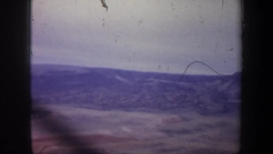 1957 Wyoming home-movie frame with a hazy ridge line, open valley ground, soft motion blur, and visible dust on the 8mm scan.