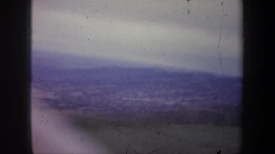 Wyoming 1957 aerial 8mm frame looking across a broad hazy valley toward distant hills, with muted color and visible film wear.