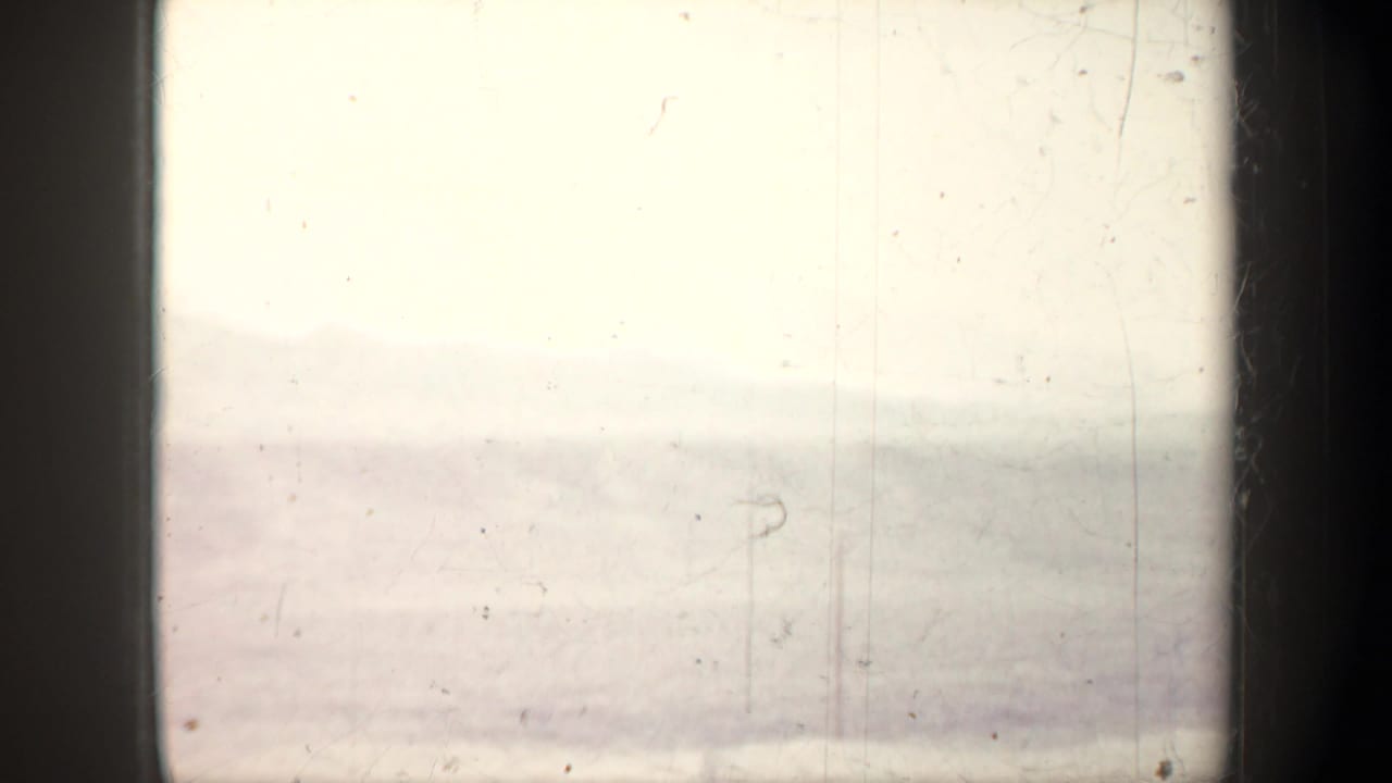 Overexposed 1957 Wyoming 8mm frame with a faint hazy horizon, possible pole shape, dust, and scratches.