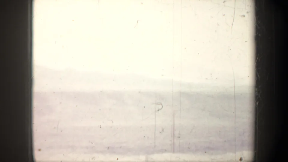 Overexposed 1957 Wyoming 8mm frame with a faint hazy horizon, possible pole shape, dust, and scratches.
