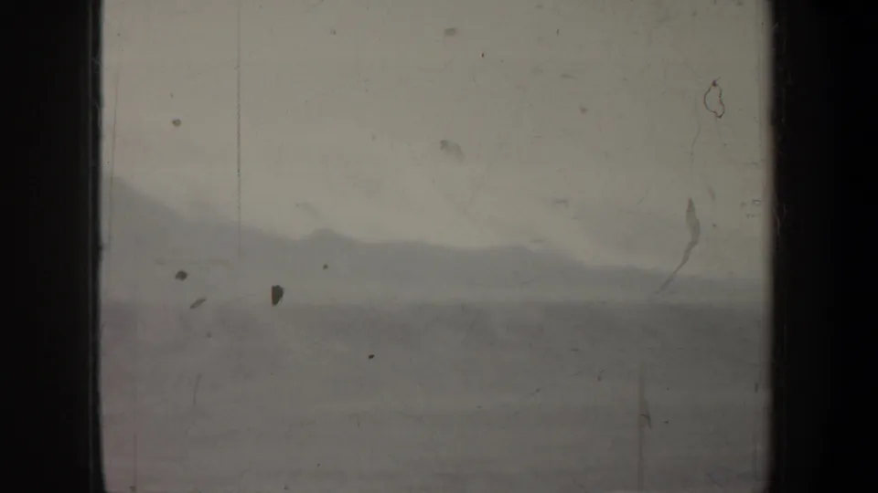 Dim 1957 Wyoming 8mm frame showing hazy mountain silhouettes beneath a pale sky, with visible dust and scratches.