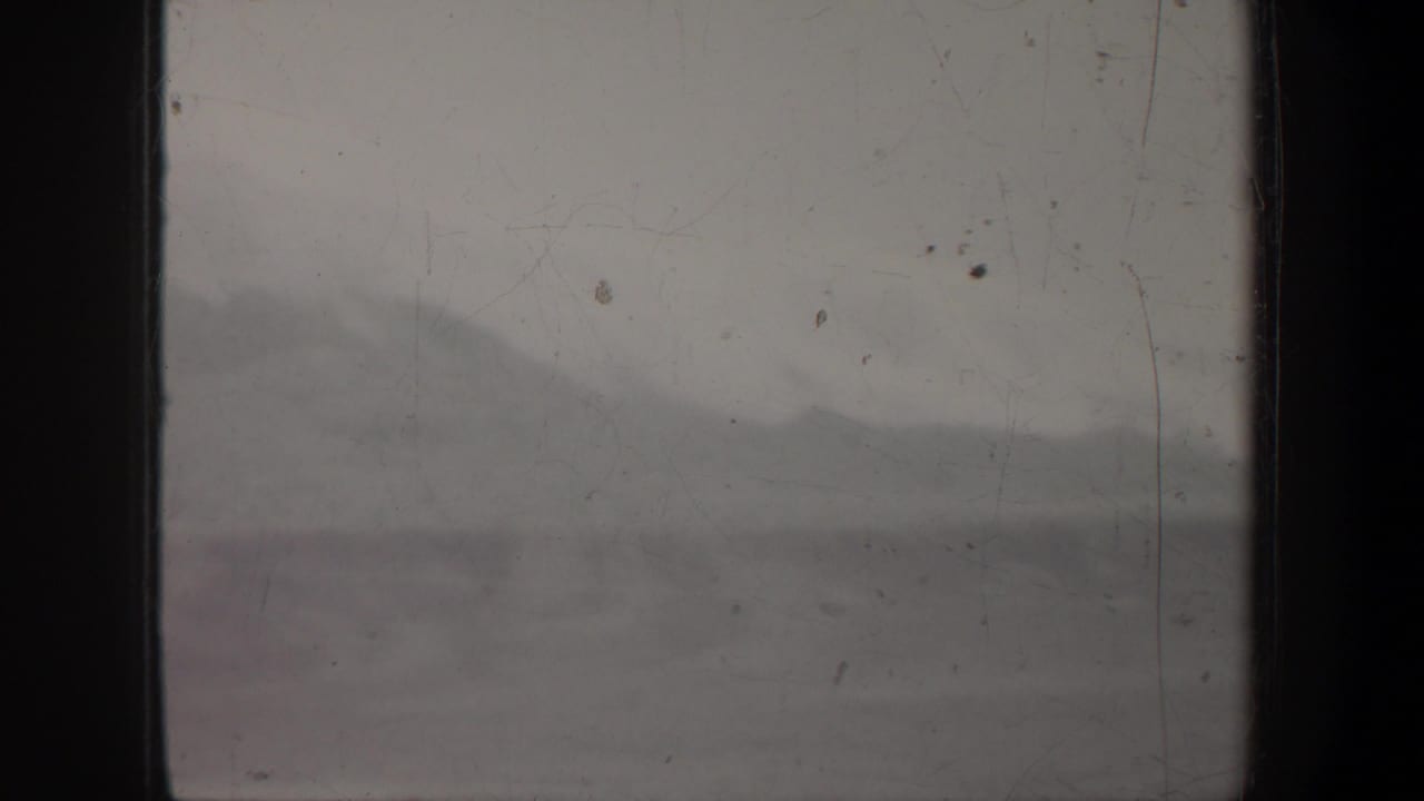 1957 Wyoming 8mm frame with a faint mountain ridge behind dark vertical bands, dust, scratches, and muted gray exposure.
