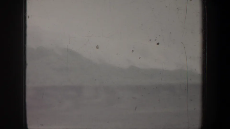 1957 Wyoming 8mm frame with a faint mountain ridge behind dark vertical bands, dust, scratches, and muted gray exposure.