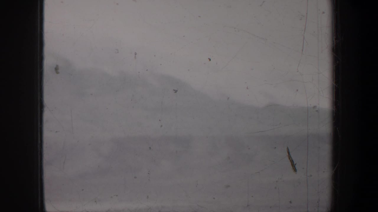 1957 Wyoming 8mm frame showing indistinct mountain ridges through a central black band, film dust, scratches, and low contrast.