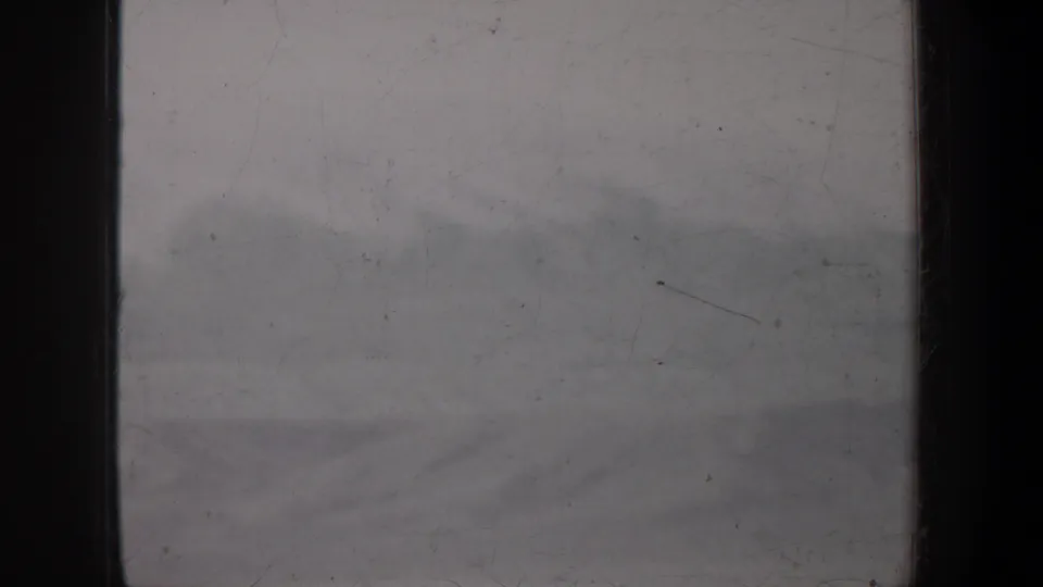 1957 Wyoming 8mm frame showing low pale clouds above small distant hills, softened by grain, dust, and scratches.