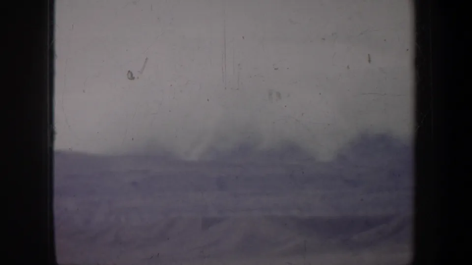 1957 Wyoming 8mm view of a low cloud bank above small distant hills, with subdued color and heavy film wear.
