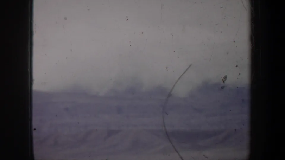 1957 Wyoming frame showing low clouds above distant hills, marked by muted 8mm color and a visible right-side scratch.