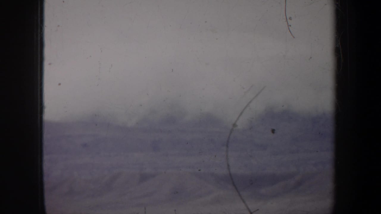 Hazy barren landscape under a pale sky with dark film edges and visible scratches.