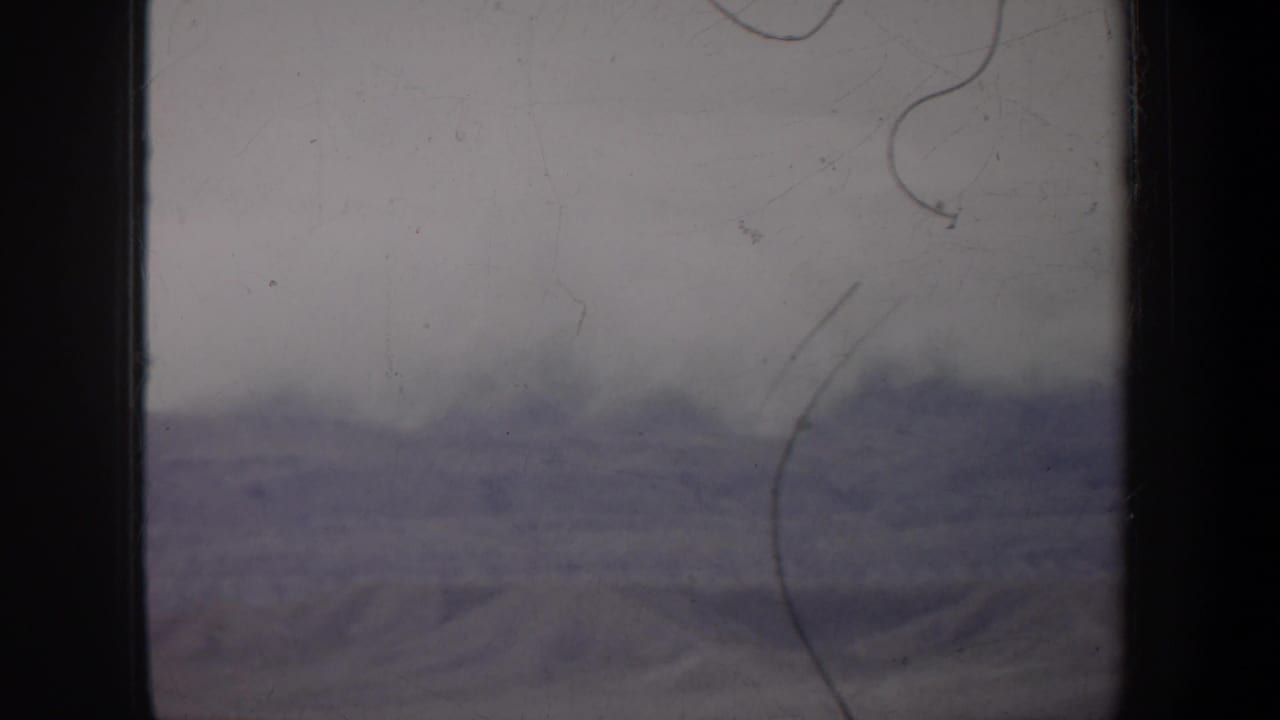 Soft distant ridges and empty ground seen through scratched, dark-edged film.