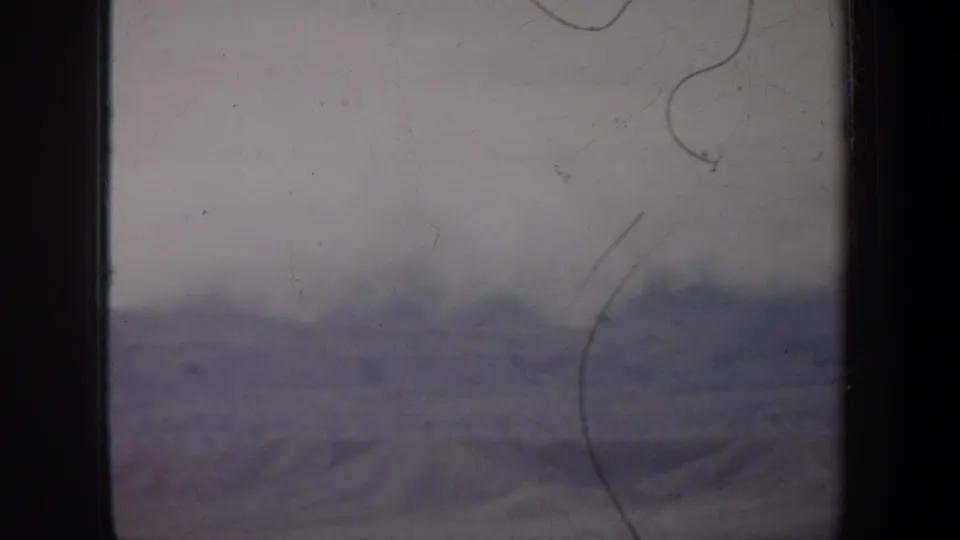 1957 Wyoming 8mm view of empty open land and low distant ridges, softened by haze, purple-gray cast, and film scratches.