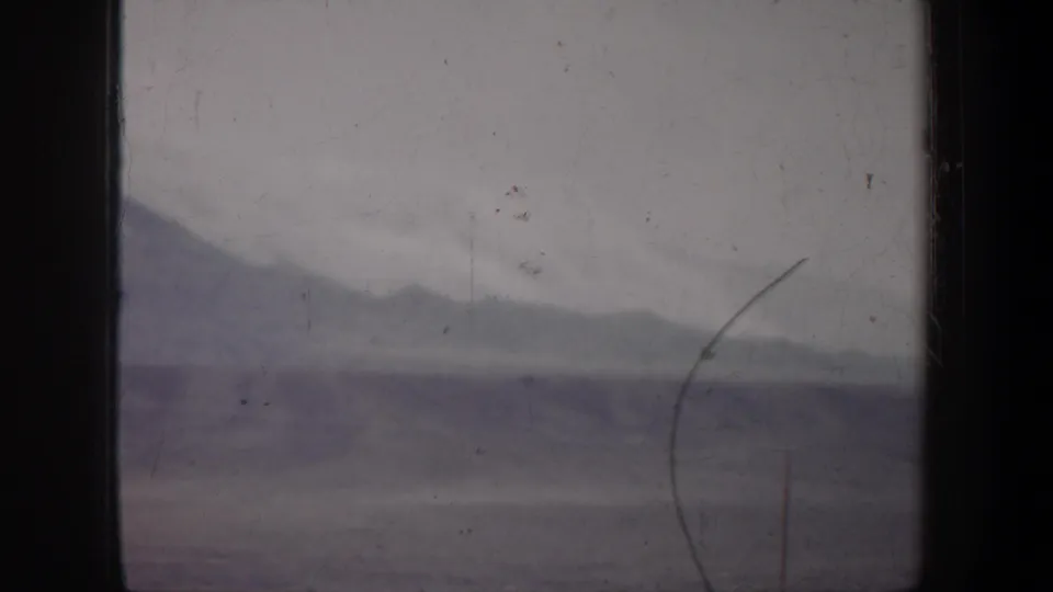 1957 Wyoming 8mm frame of sparse open terrain and a low horizon, with a curved branch or scratch visible in the foreground.