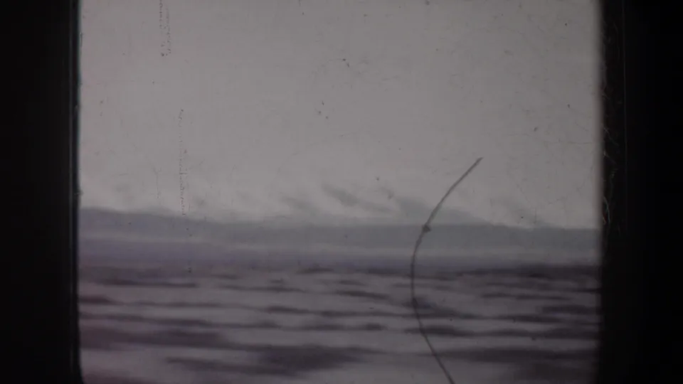 1957 Wyoming 8mm view of flat open terrain, distant haze, and a pale sky, framed by dark film edges and surface wear.