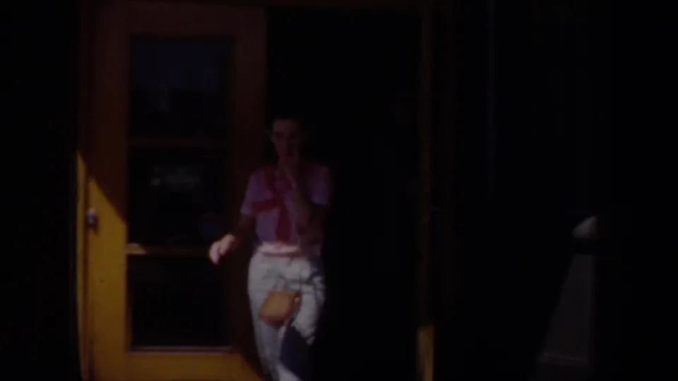 An adult woman stands by a yellow doorway, partly shadowed, in a 1957 Wyoming home-movie frame.