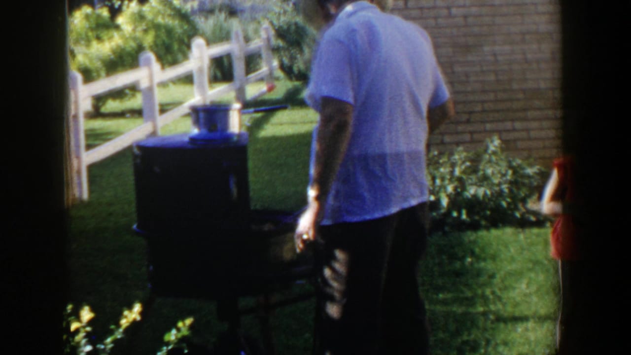 Man seen from behind near a grill with a pot on top beside a white fence.