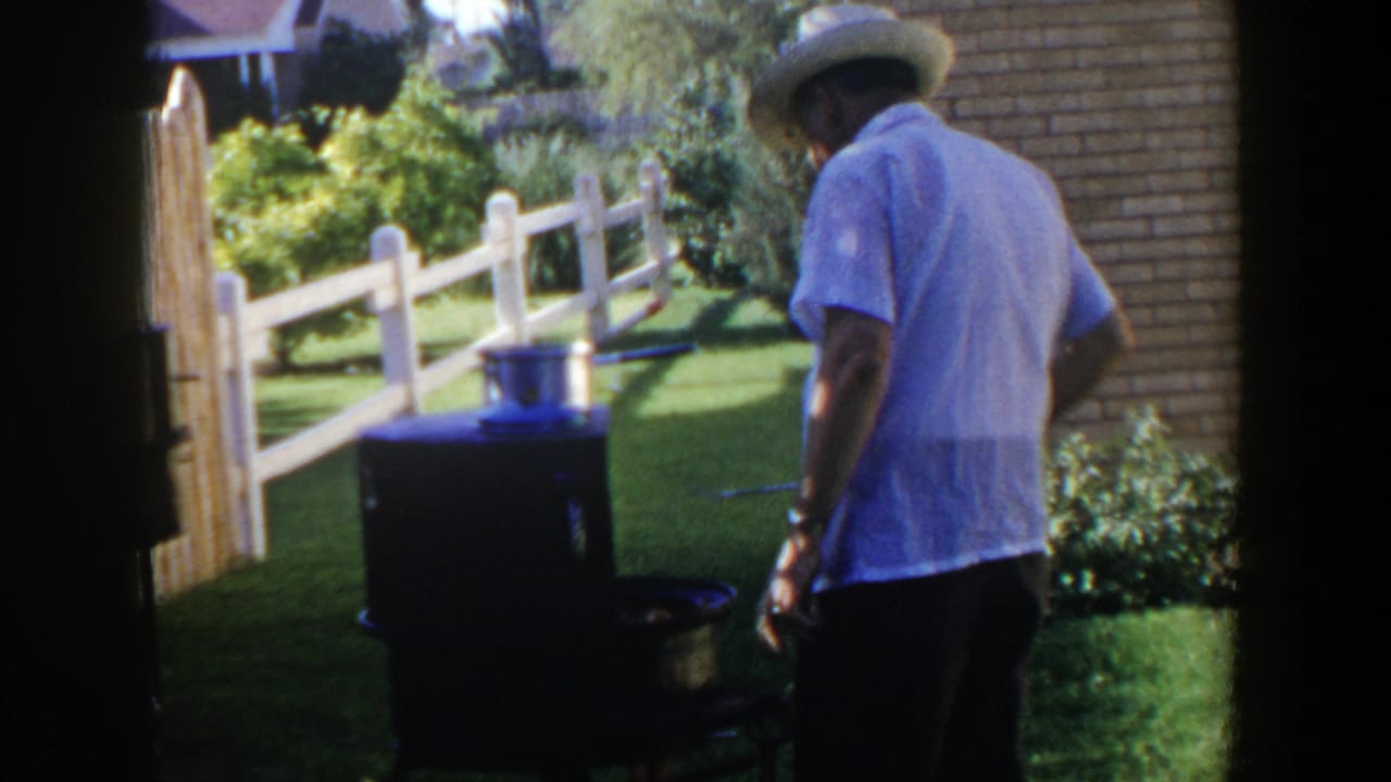 In likely 1953 Lubbock backyard footage, a man in a straw hat stands beside a dark outdoor grill with a pot on top.