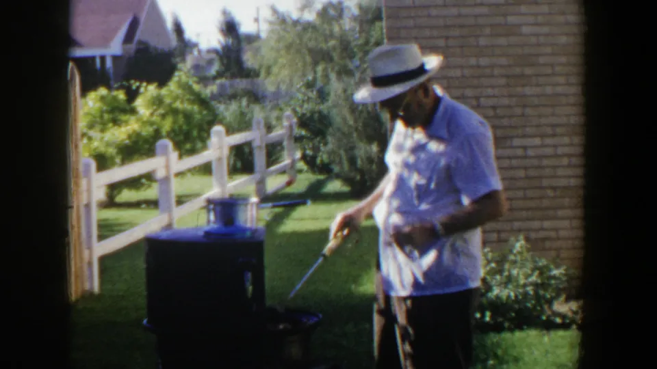 In 1953 Lubbock home-movie footage, an older man in a white hat stands beside a portable cooker in a green backyard.