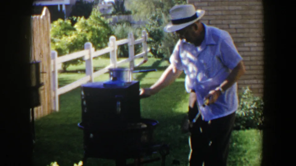 In the final frame, the man leans toward the cooker as sunlight falls across the lawn, fence, and brick wall.