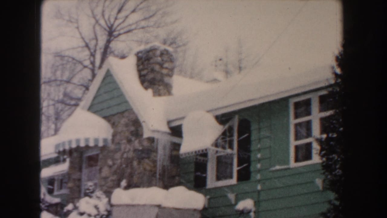 Closer view of the snowy green house with open window area, stone chimney, awning, and icicles.