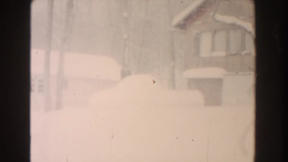 Faded 8mm frame of a Dearborn winter house exterior, with deep snow, bare trees, and a bright hazy exposure.