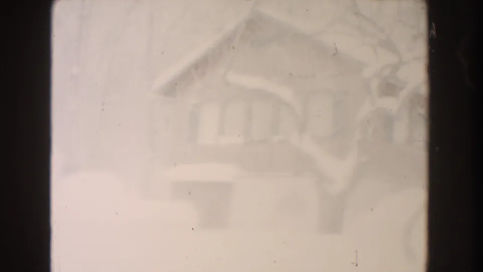 1961 Dearborn frame showing a softly exposed snow-covered house exterior, bare tree branches, and a dark lower window or opening.