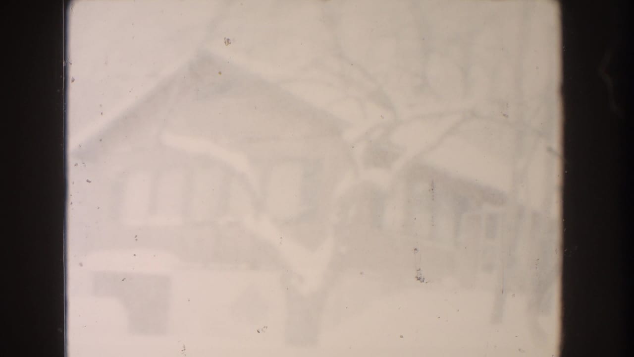 Soft, hazy snow-covered residential view with bare tree shapes and dark film edges.