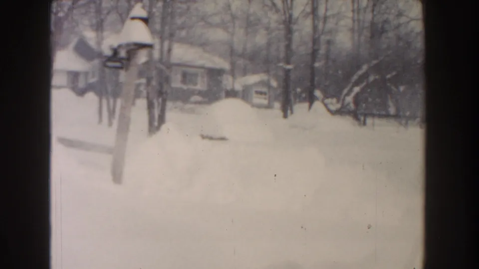1961 Dearborn winter yard view with deep snow, a small yard fixture, bare trees, and neighboring houses in the background.