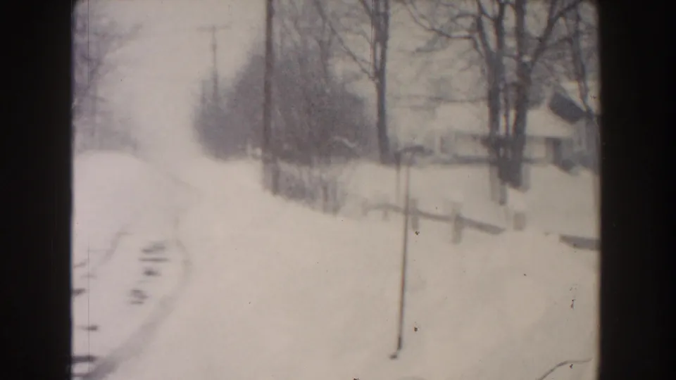 1961 Dearborn, Michigan winter frame with a snow-covered road, tire tracks, bare trees, utility poles, fencing, and a small house.