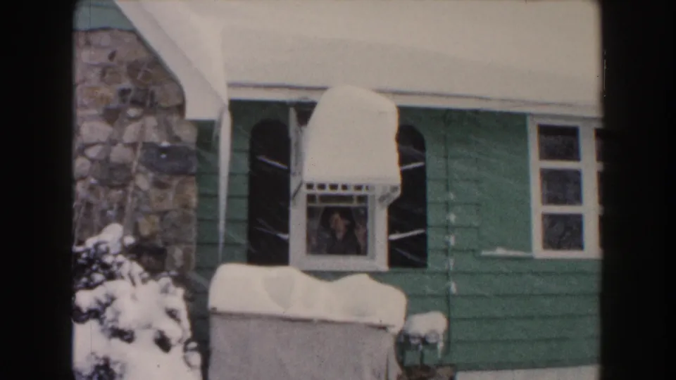 1961 Dearborn frame of the green house facade, with snow on the awning and a person looking from the window.