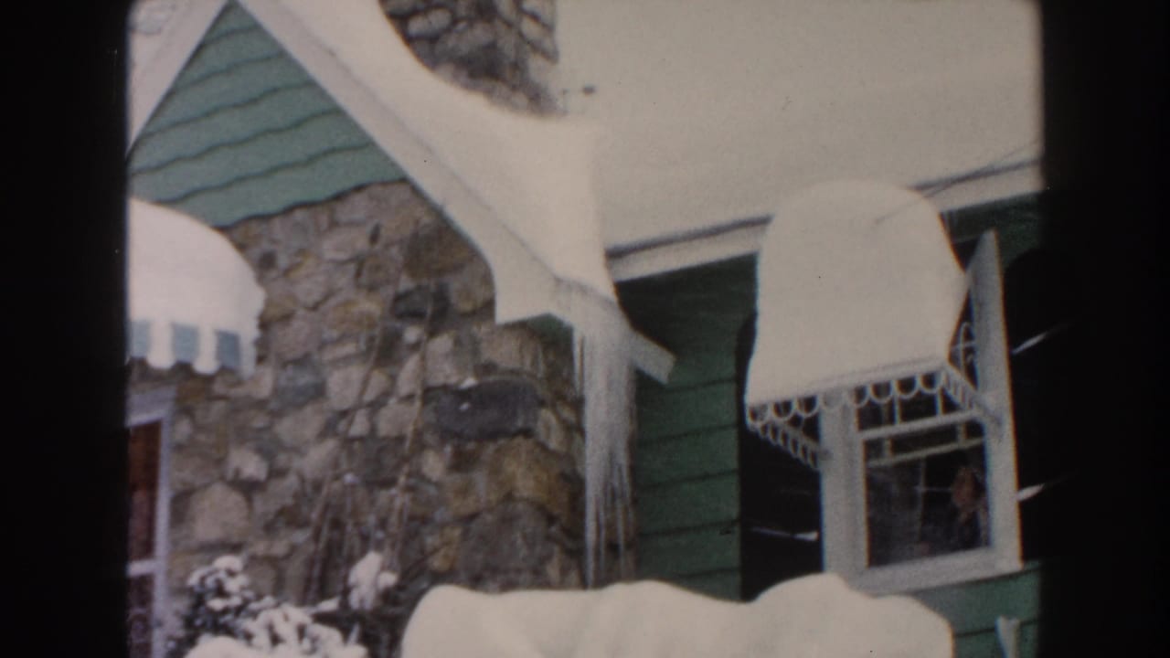 Snowy house exterior with stone wall, green siding, awning, icicles, and a window.