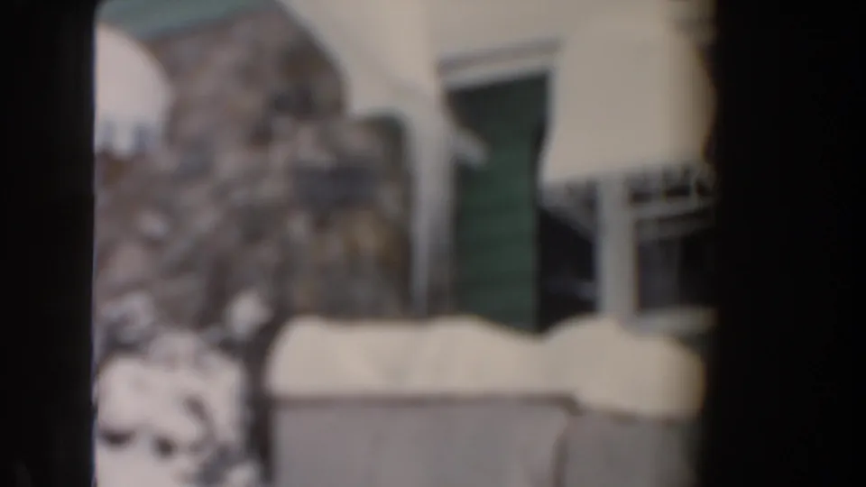 Soft-focus 1961 Dearborn winter frame showing the green and stone house exterior under snow.