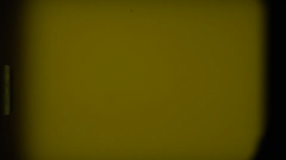 1973 8mm frame from Florida showing a dark foreground edge, a gray car, and a house with a white vehicle in the driveway.