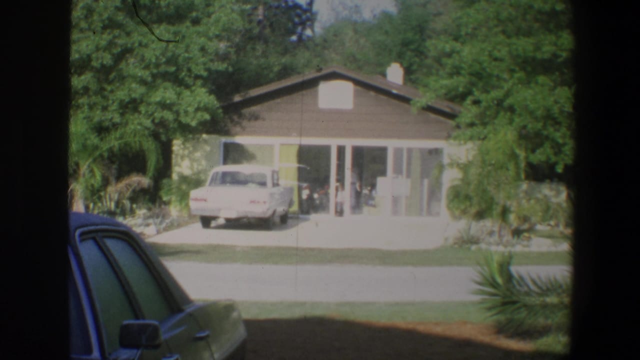 Bungalow with glass doors and a white car parked in the driveway, seen through a dark foreground frame.