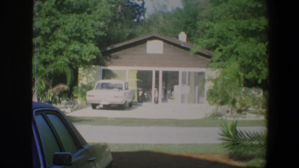 1973 Florida residential exterior at Walt Disney World area with a white car in the driveway and people faintly visible near glass doors.
