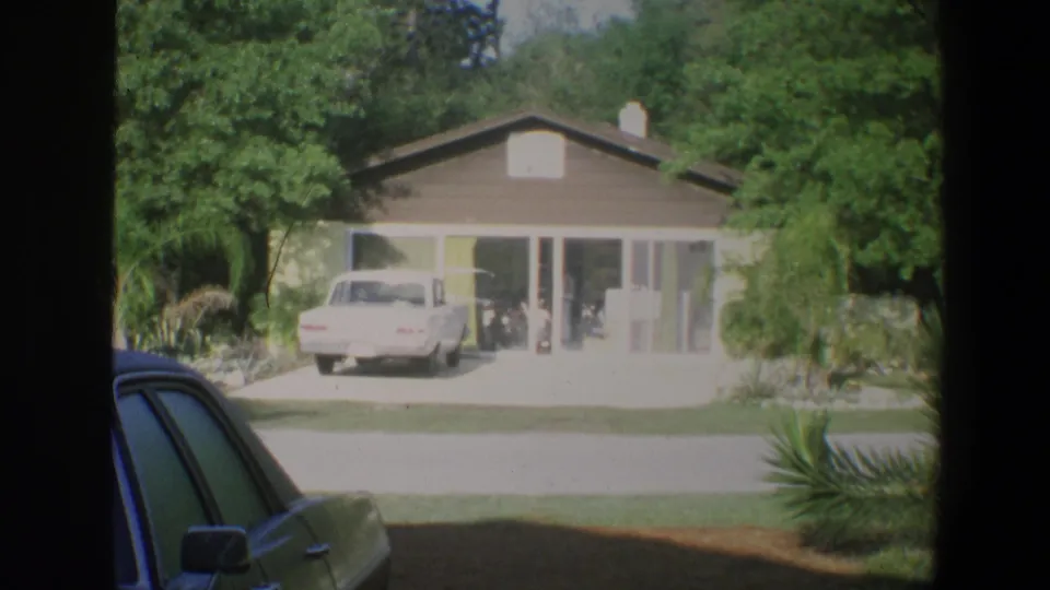 1973 Walt Disney World Florida home-movie view of a landscaped bungalow with a white car parked before glass doors.