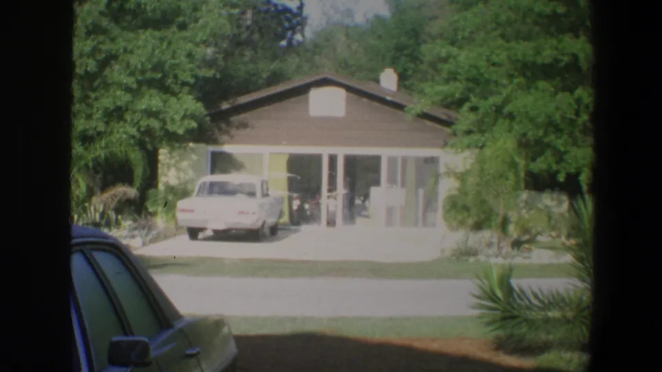 1973 Florida home-movie frame of a bungalow and driveway at Walt Disney World, with faint figures near the glass entrance.