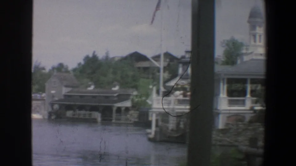The 1973 Walt Disney World view shows waterfront buildings, a pier or dock, trees, and a partially visible tower from across the water.