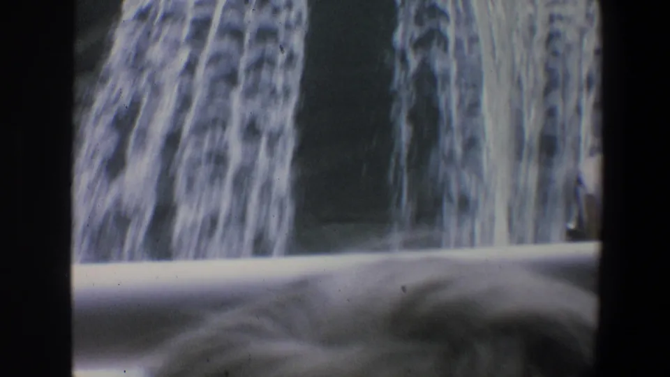 1973 Walt Disney World home-movie frame showing a waterfall-like cascade, pale foreground barrier, and dark vertical film borders.