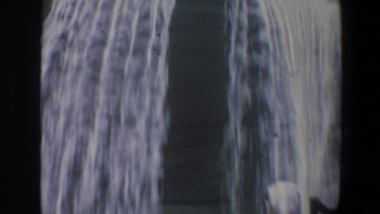 Close view of falling water beside a dark vertical shape and film-frame border.