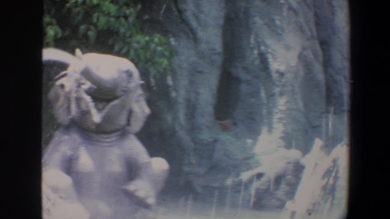 1973 Walt Disney World home-movie frame showing an elephant figure with its trunk raised near rockwork and foliage.